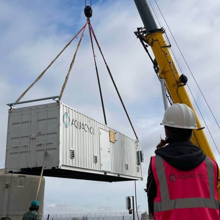 Aquacycl service person installing a new wastewater treatment system with the container hauled on a crane in background